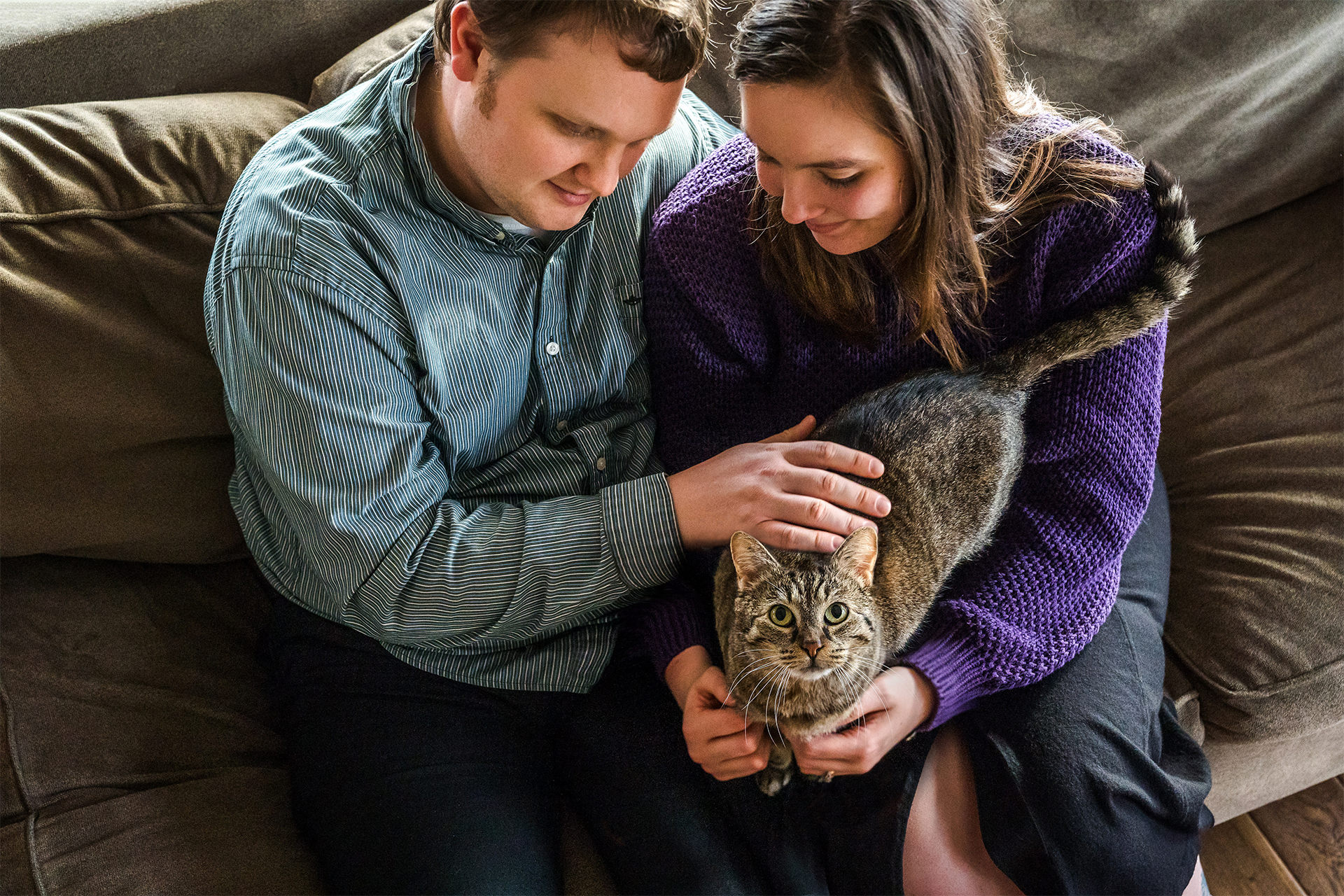 A couple sits on their couch with their cat