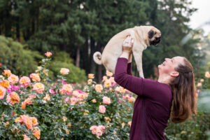 Woman holds up pug at the International Rose Test Garden