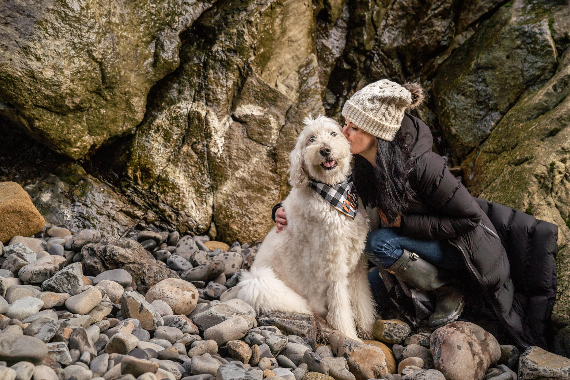 Woman kisses her dog on the beach rocks
