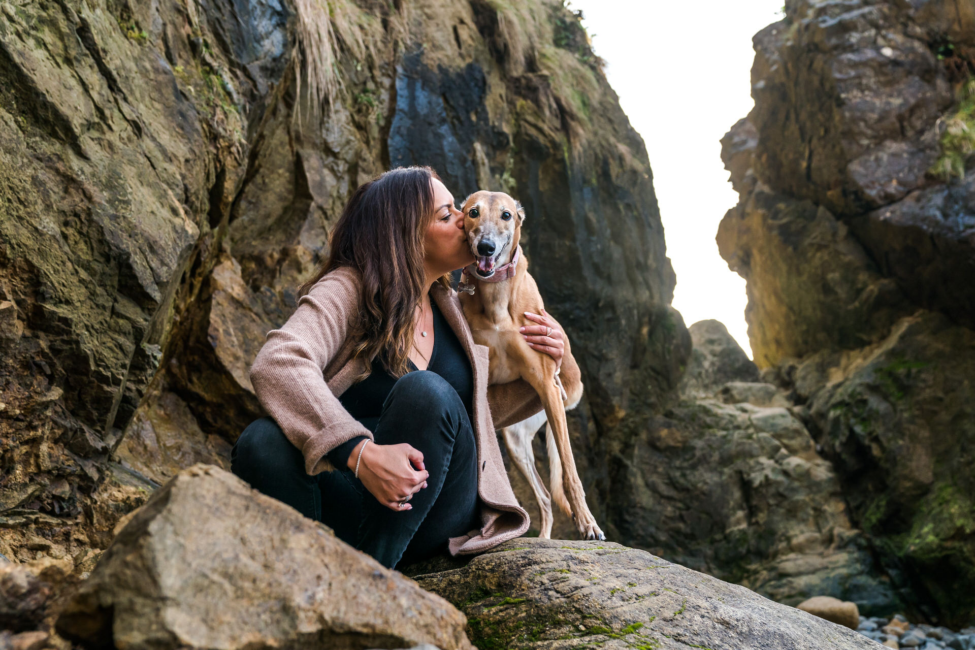 woman kisses her dog on rocky beach