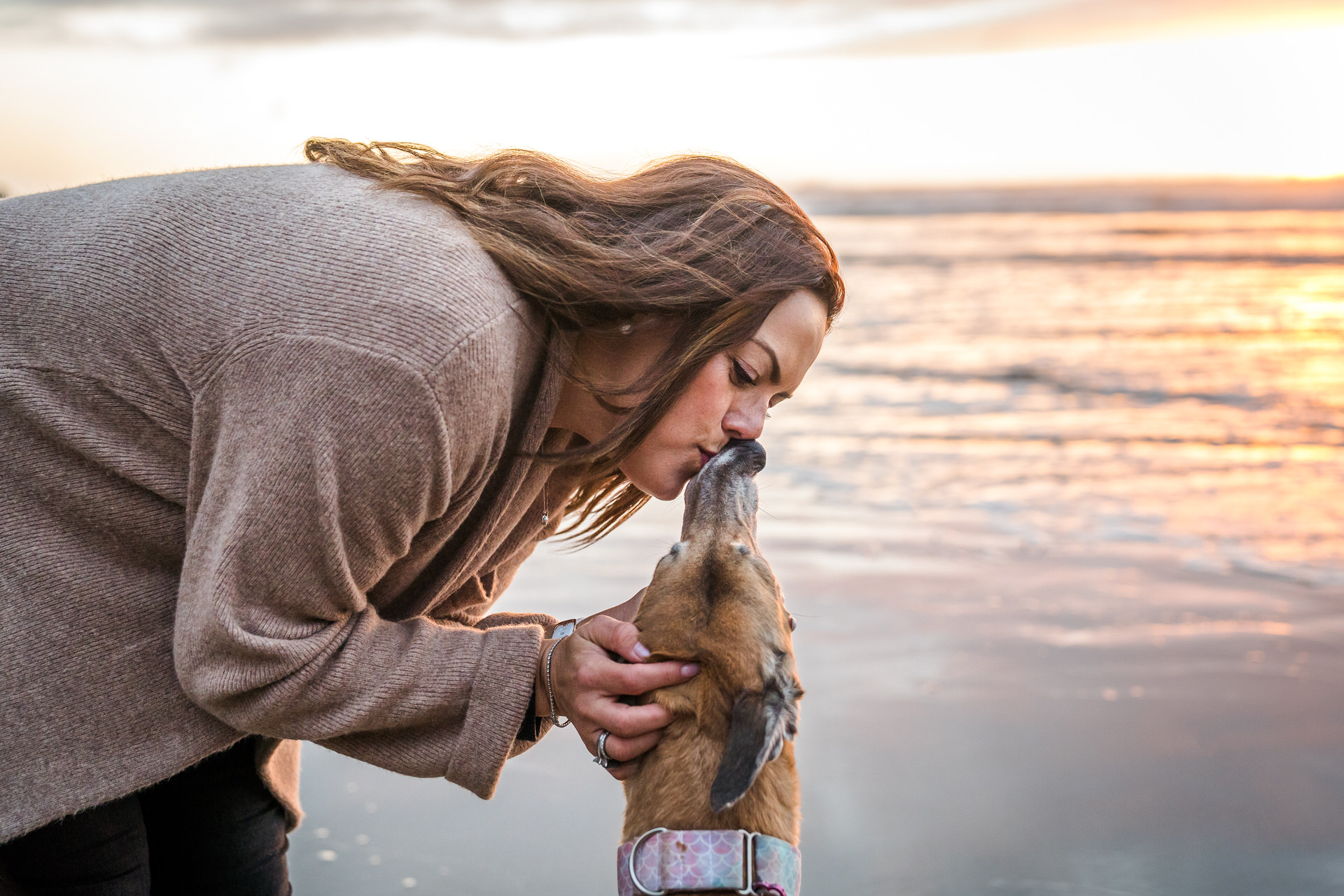 woman kisses her dog at sunset