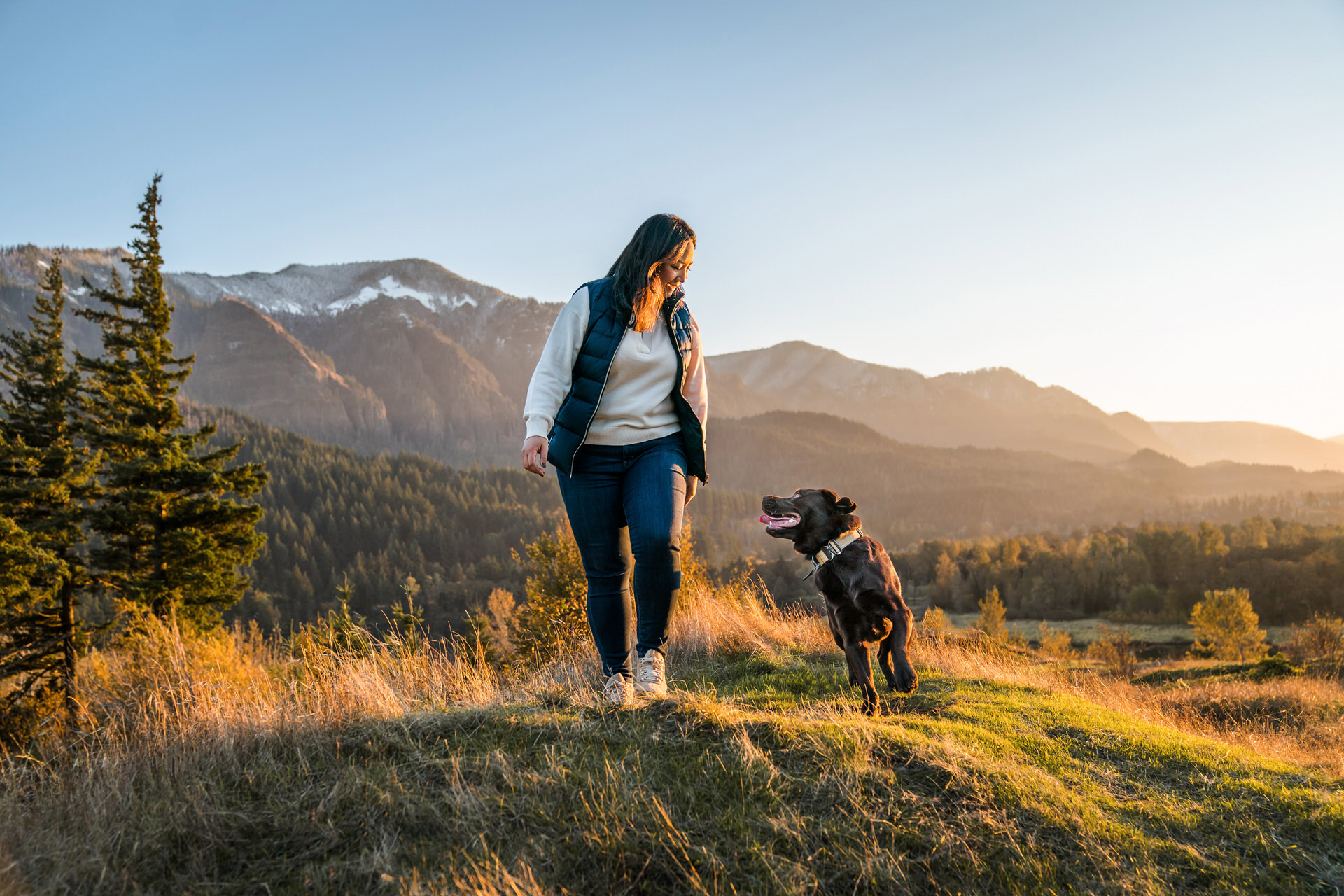 woman and dog walk together in beautiful sunset light in the mountains