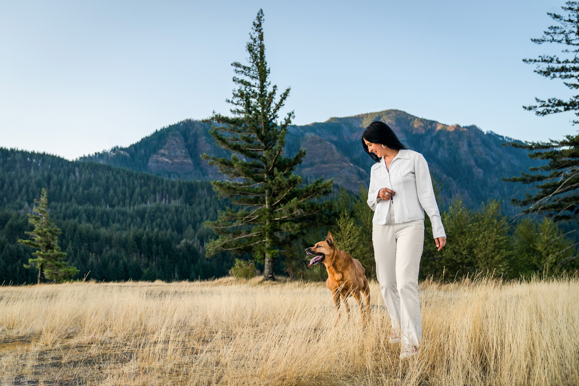 woman walks through field of tall grass with dog