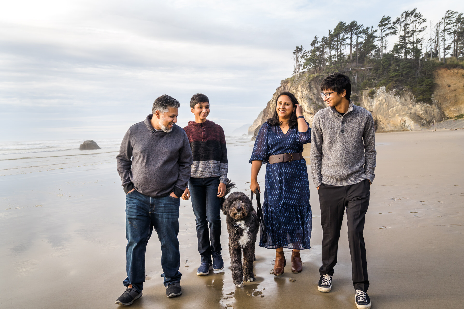 Family with two teenage sons and a dog walk on the beach in Arch Cape, Oregon