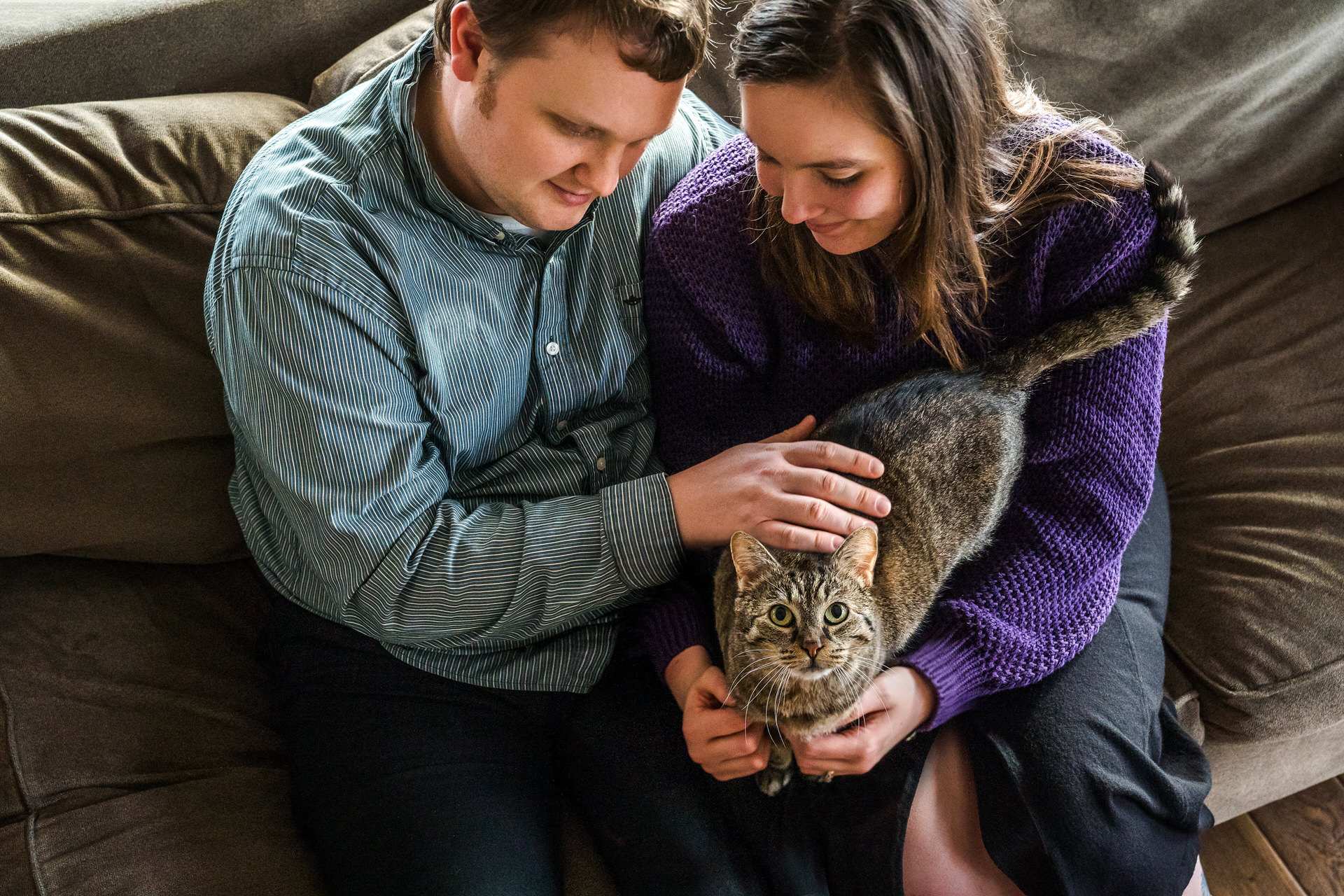 A couple sits with their cat on a couch