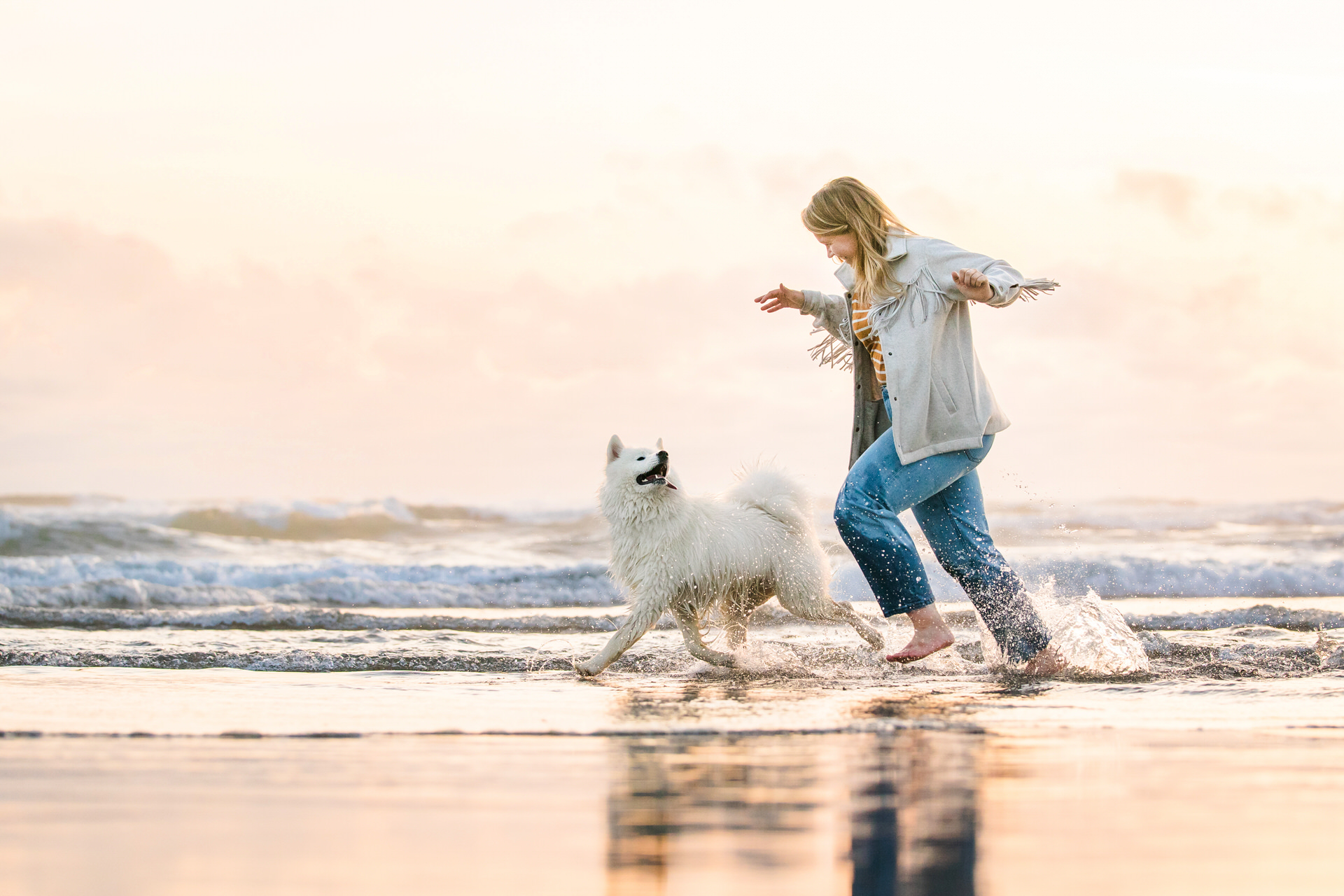 dog and woman running together and playing in the ocean